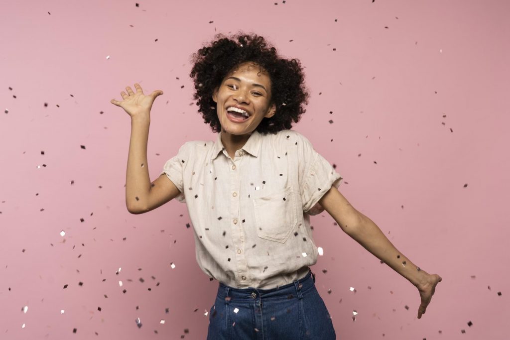 A woman standing in front of pink wall with confetti.